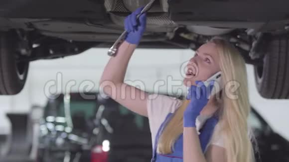 白种人女汽车修理工拧紧螺丝和在电话上交谈的肖像穿蓝色工作服的金发女人视频的预览图