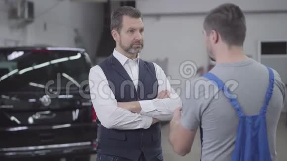 不满意的白种人成年男子在修理店与汽车修理工交谈的肖像英俊的商人不高兴视频的预览图