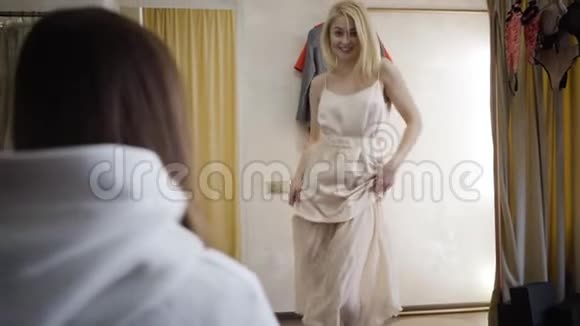 一幅年轻的金发女郎穿着优雅的米色裙子旋转的肖像无法辨认的支持高加索人的朋友视频的预览图