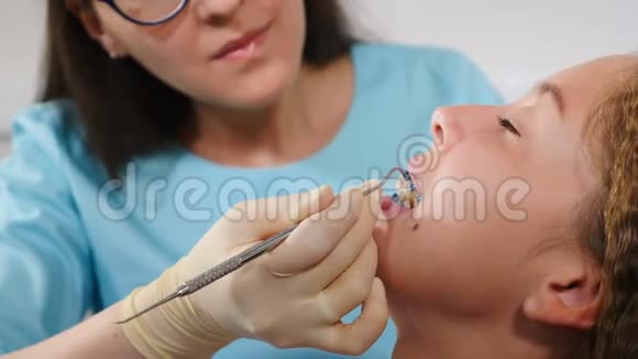 微笑的女正畸医生在牙科办公室检查孩子特写镜头现代戴牙套的漂亮女孩视频的预览图