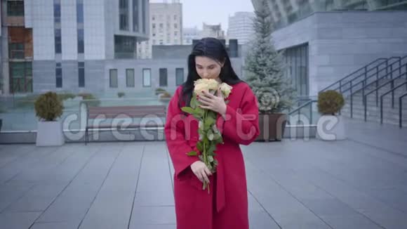 镜头接近快乐的年轻女士闻到黄色玫瑰下的小雨在城市美丽的白人女子视频的预览图