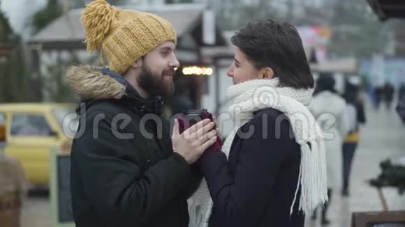 侧观恋爱中的男人和女人站在冬季集市上互相看着抱着一个视频的预览图