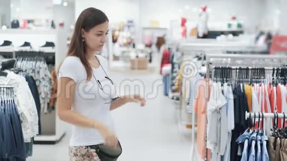 年轻女子在商场购物为孩子挑选衣服看尺寸视频的预览图