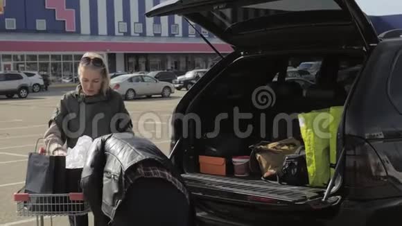 汽车附近的一对夫妇把购物袋从篮子里卸到后备箱里视频的预览图