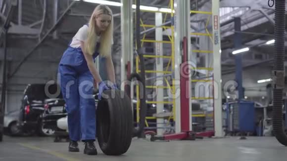 年轻的白种人女人在修理店滚动轮胎在工作场所微笑的女汽车修理工摄像机放大了视频的预览图