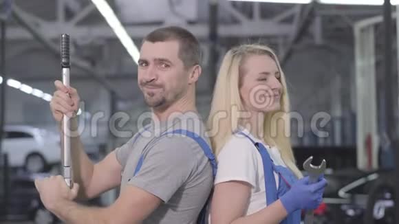 开朗的白种人男人和女人背靠背站着看着相机微笑着快乐汽车机械师摆姿势视频的预览图