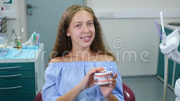 微笑的女孩带着矫形牙套在牙科椅上保健牙科保健和牙科概念年轻快乐视频的预览图