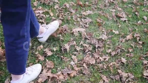 一个女孩穿着牛仔裤和运动鞋走在草坪上温暖的冬天秋天天气没有袜子的脚踝视频的预览图