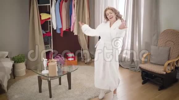 高瞻远瞩的照片年轻的白种人女孩在家跳舞的感觉穿着白色浴袍享受音乐的快乐女人视频的预览图