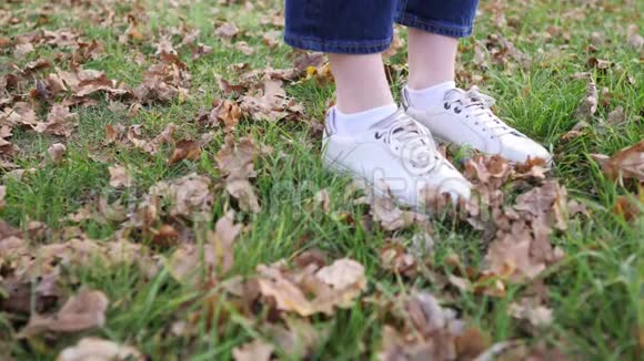 女人脚穿着白色的运动鞋在绿草上落叶静态特写镜头秋季自然视频的预览图