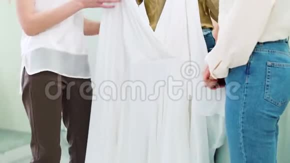 年轻的新娘和女性朋友在婚纱沙龙里试穿婚纱视频的预览图
