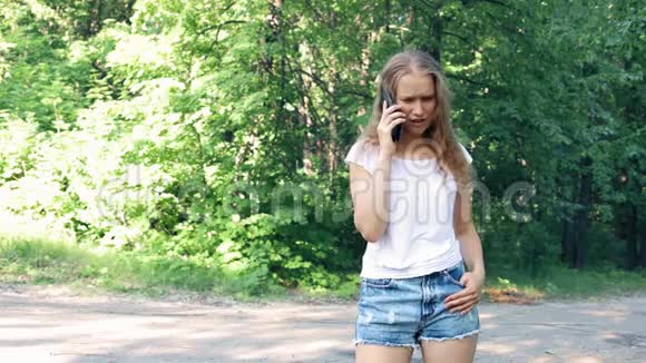 在公园树的背景下一个激动的女孩在手机上说着话视频的预览图