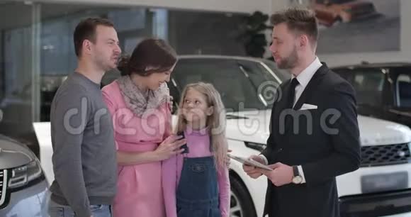 一名成年白人男子在汽车经销店与商人交谈抚摸女儿的下巴年轻家庭选车视频的预览图