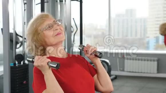 积极的退休人员在健身俱乐部用哑铃做轻操有杠铃的资深退休妇女视频的预览图
