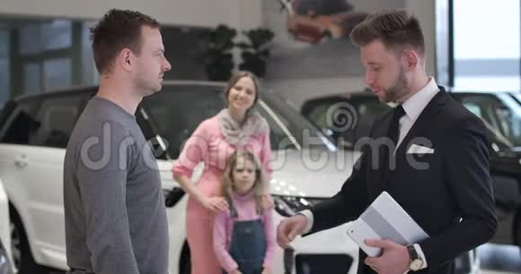 快乐的白种人母女在他们的丈夫和父亲拿着车钥匙的背景下做胜利的手势视频的预览图