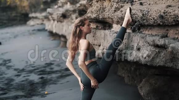年轻女子在悬崖附近的黑色沙滩上做伸展运动视频的预览图