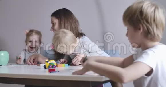开朗的金发碧眼的姐妹在后台和妈妈玩耍可爱的男生在右边画画幸福家庭视频的预览图