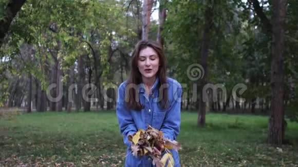 秋天公园里一位美丽的年轻女子把落叶扔在树上快乐与乐趣甜蜜视频的预览图