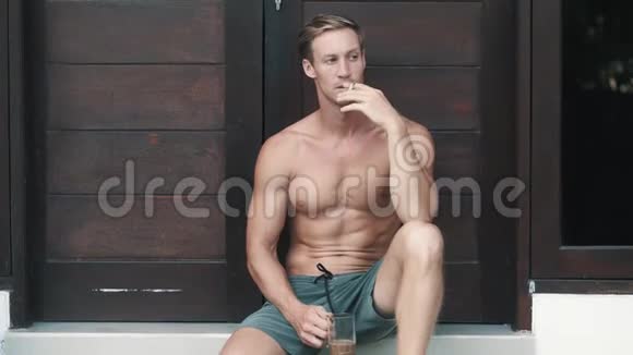 性感男人坐在别墅的木门旁抽烟喝咖啡视频的预览图