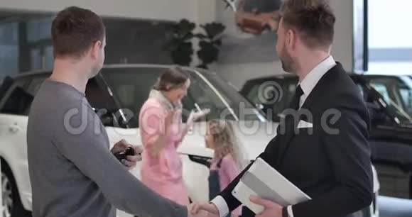 快乐的白人小女孩从后台跑到父亲买新汽车和拿汽车钥匙成功视频的预览图