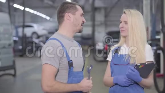 两个专业的汽车机械师说话转向相机和微笑的肖像穿着蓝色长袍的男人和女人视频的预览图