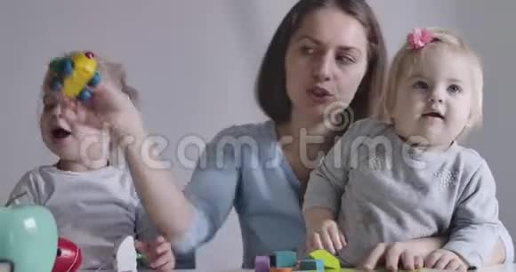 快乐的黑发白种人女人和两个女儿玩玩具的肖像可爱的积极的女婴和视频的预览图