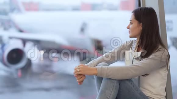 年轻女子坐在靠近窗户的机场背景模糊的飞机视频的预览图