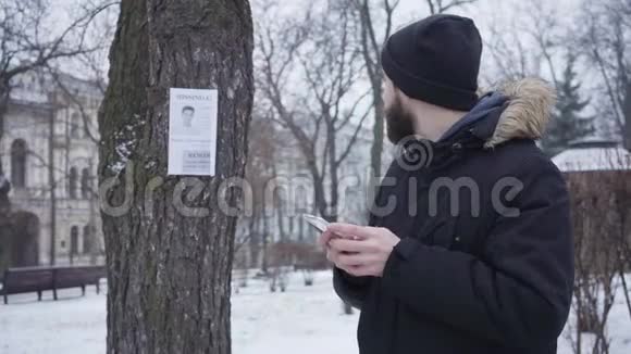 一张留胡子的白种人年轻男子的肖像站在失踪儿童广告旁边打电话帅哥提供视频的预览图