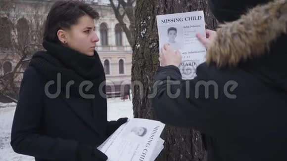 白人男子把失踪的儿子广告挂在树上因为他沮丧的妻子站在其他小册子上离开镜头的人视频的预览图