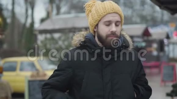 年轻的冻白种人站在户外穿着温暖的衣服在智能手机上检查时间有胡子的家伙视频的预览图