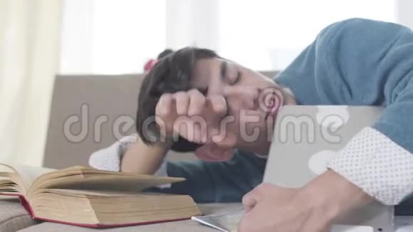 用书和平板电脑睡在沙发上的年轻白种人男孩的特写肖像精疲力竭的男大学生视频的预览图