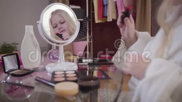 快乐的白种人女孩在镜子前涂红口红可爱的金发孩子在室内使用化妆品视频的预览图