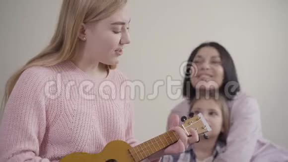 可爱的金发白种人女孩为母亲和妹妹演奏四弦琴唱歌天才少年视频的预览图