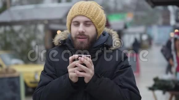白种人成年男子的肖像棕色的眼睛站在冬季集市上喝咖啡带着黄色微笑的年轻人视频的预览图