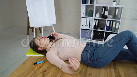 年轻的女商人躺在桌子上在办公室打电话视频的预览图
