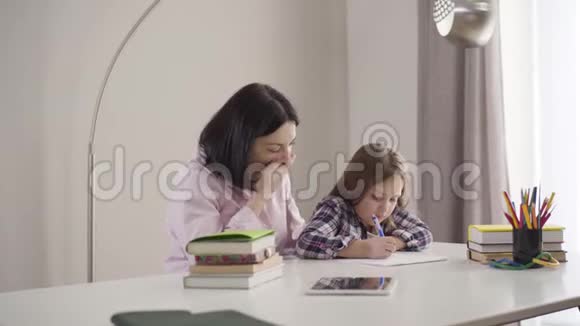 镜头接近疲惫的白种人母亲打哈欠帮助女儿做家庭作业可爱的黑发女生视频的预览图