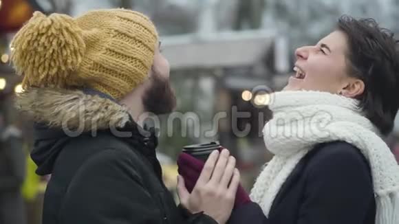 侧面的肖像开朗的白人男女站着咖啡杯在冬季博览会和笑声年轻快乐视频的预览图
