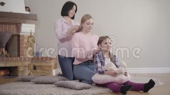 母亲一边给大女儿编辫子一边给小女孩编辫子快乐的白种人家庭在一起休息视频的预览图