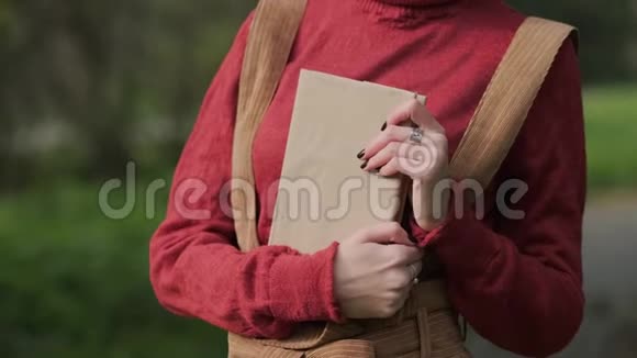 年轻迷人的红头发女人戴着帽子和毛衣在自然公园的长凳上看书秋天凉爽的一天视频的预览图