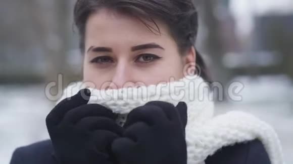 棕色眼睛的白种人年轻女孩的特写脸上藏着白色温暖的围巾可爱女人的肖像视频的预览图