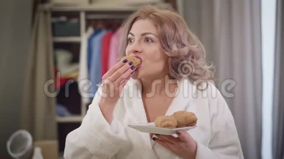 饥饿美丽的白种人女孩喜欢吃羊角面包的肖像年轻女子在家嚼着美味的面包饮食食物视频的预览图