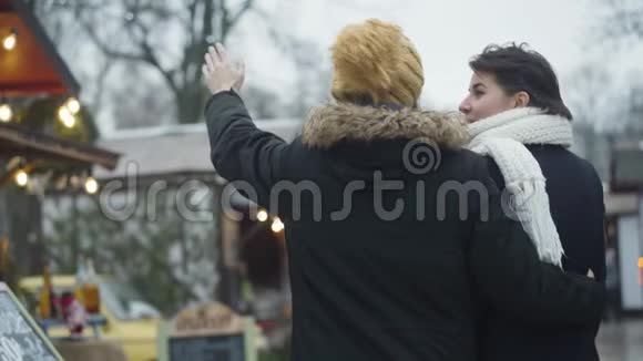 回到快乐的白种人夫妇站在冬季集市和谈话年轻人在炫耀什么女人视频的预览图