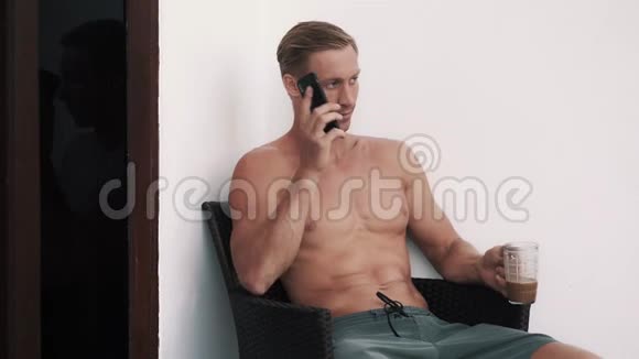 性感男人坐在户外的扶手椅上在电话里谈笑风生视频的预览图