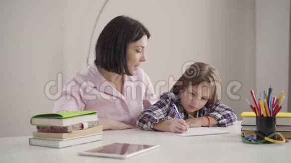 年轻的白种人母亲对女儿发号施令就像漂亮的黑发女孩写下来一样小学生做作业视频的预览图