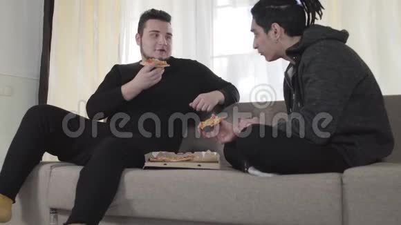 两个年轻的白人男性朋友吃披萨和聊天成年大学生周末在室内休息视频的预览图