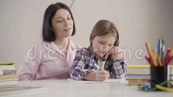 白种人成年女性和女儿坐在餐桌上的肖像家长帮助女学生做作业学习视频的预览图