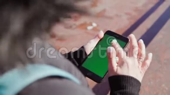 女孩手里拿着一部智能手机手里拿着一个绿色的屏幕在手机里沿着街道攀爬对Steadicam的射击视频的预览图