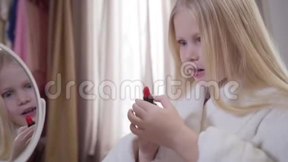 金发白种人女孩的特写打开红色口红摇头穿白色浴袍的时髦漂亮孩子视频的预览图