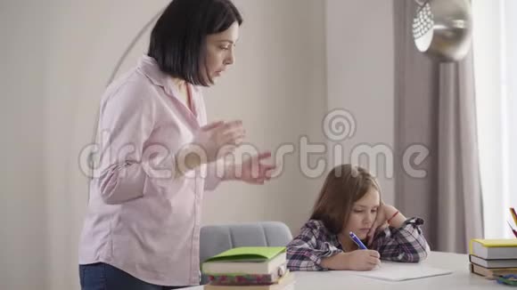 从侧面看黑种人白种人的女人对坐在桌子旁的漂亮女学生大喊大叫扰乱孩子做作业视频的预览图