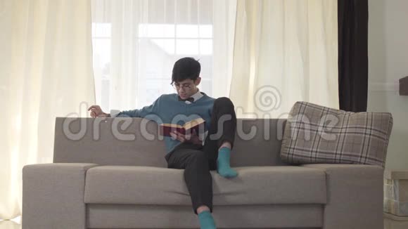 专注的白人年轻人坐在沙发上看书的肖像英俊的大学生周末休息视频的预览图